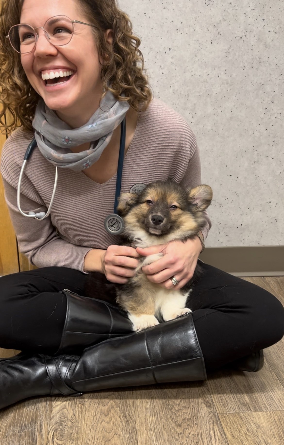 A woman in black boots and a scarf gently holds a cute puppy in her arms, forming a heartwarming bond.