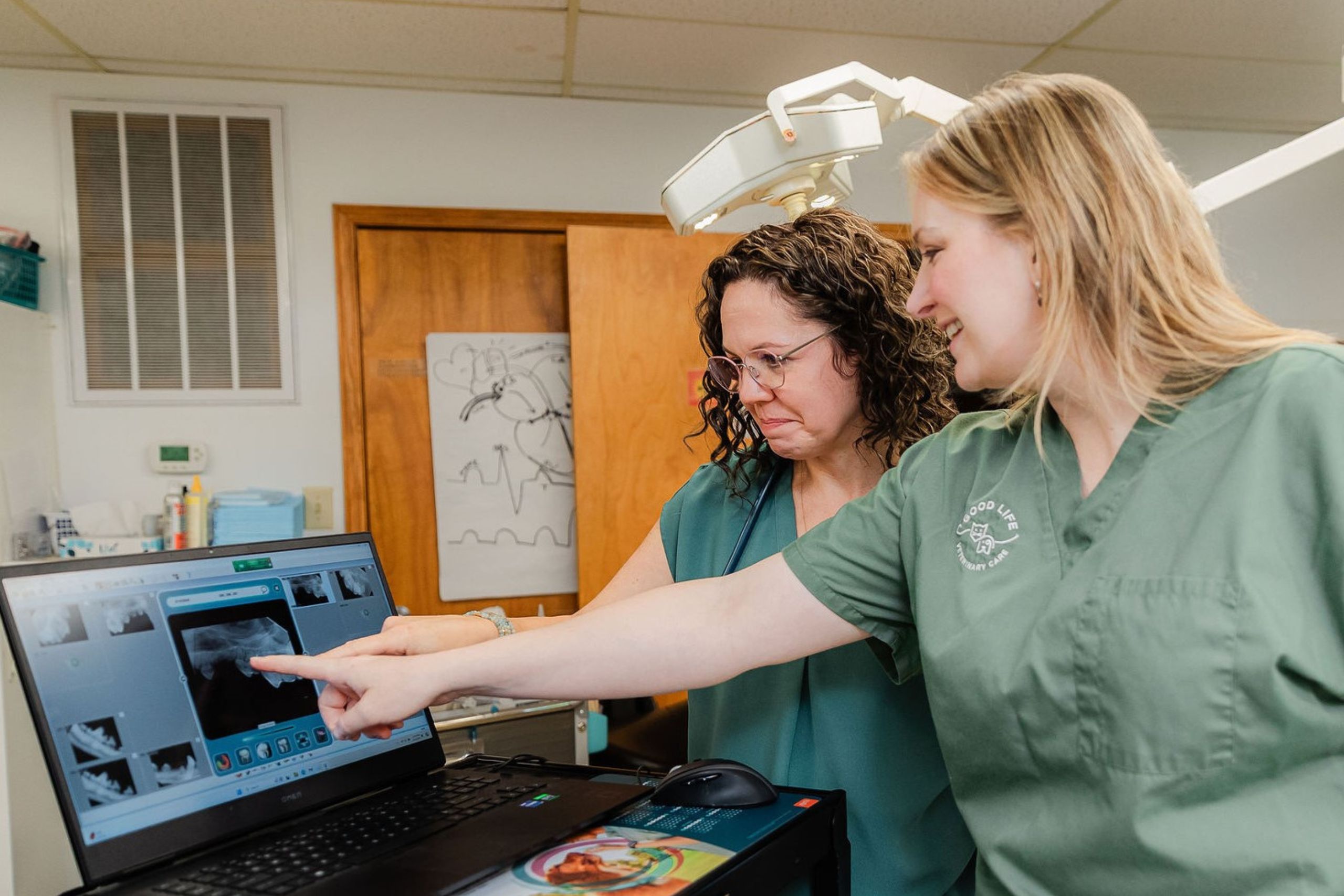 Two women in green scrub shirts focused on a laptop screen